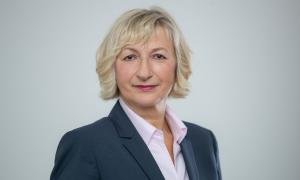 Eine Frau mit kinnlangen Haaren und einem Pony. Sie schaut direkt in die Kamera und trägt eine Anzugsjacke und ein Hemd.