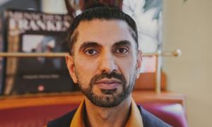 Ein Mann mit kurzem Bart und kurzen, zusammengebundenen Haaren schaut in den Betrachter direkt an.. 