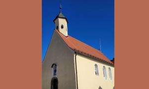Die Peterskapelle ist ein schlichtes Gebäude. Sie hat nur einen einzelnen Kirchturm auf ihrem Satteldach. Im Hintergrund ist wolkenloser Himmel.