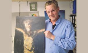 Ein Mann hält ein Bild, das einen gekreuzigten Jesus zeigt, in die Kamera.