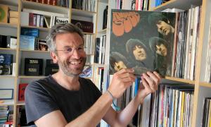 Ein Mann vor einem Plattenregal, das Beatles-Album "Rubber Soul" in den Händen, er grinst