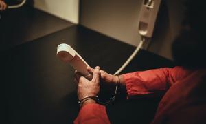 Ein Mensch in einem orangenen Anzug und Handschellen hält ein Telefon in der Hand.