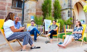Eine Gruppe Menschen sitzt in Liegenstühlen, die auf Sand vor einer Kirche stehen