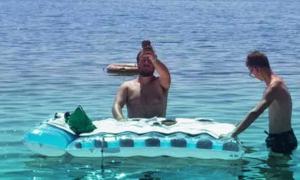 Ein Mann steht im Wasser, vor ihm eine Luftmatratze, die ein Jugendlicher hält