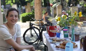 Eine Frau an einem Tisch mit Kuchen, im Hintergrund Grabsteine