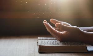 Eine Bibel liegt auf einem Tisch. Zwei Handy liegen darauf und zeigen zum Himmel.