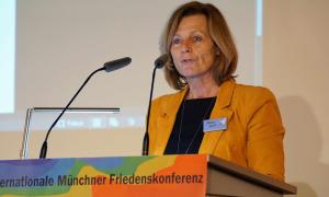 Eine Frau im orangenen Blazer steht am Rednerpult