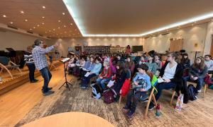 Ein Kinderchor auf Stühlen, davor ein Dirigent am Pult
