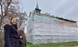 Zwei Menschen stehen vor einer Kapelle mit Gerüst