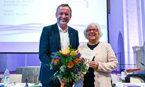 Ein Mann steht neben einer Frau. Er hält in der Hand einen Blumenstrauß