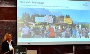 Eine Frau am Rednerpult, hinter ihr eine Präsentation mit der Überschrift "Quo vadis Tourismus?"