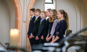 Jugendliche stehen in festlicher Kleidung mit gefalteten Händen in einer Reihe