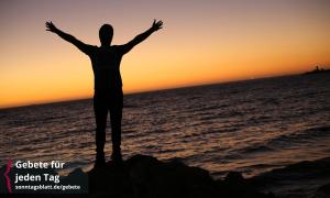 Ein Mensch steht am Meer und hebt die Arme