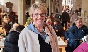 Eine Frau mit Brille, dahinter sitzen Menschen an Tischen