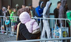 Eine Frau hält ein kleines Kind auf dem Arm, dahinter Menschen in einer Schlange hinter Absperrgittern