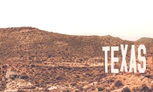 Man sieht einen großen Sandberg, der sich über das ganz Bild zieht. Er ist nicht besonders hoch. Auf ihm wächst viel trockenes Gestrüpp. Rechts im Bild steht in großen dreidimensionalen Buchstaben "TEXAS"