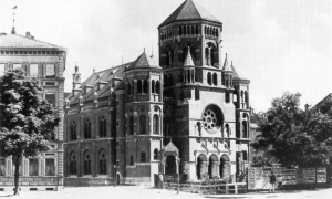 Auf dem Schwarz-Weiß-Bild erkennt man einen Flügel sowie die Front einer großen Synagoge. Links neben ihr bahnt sich ein weiteres großes Haus an. 