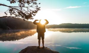 Ein Mensch steht vor einem Sonnenaufgang am Wasser