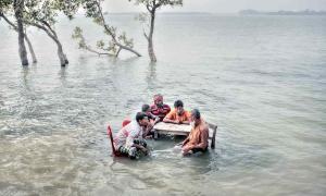 Fünf dunkelhäutige Menschen sitzen im Wasser an einem Tisch