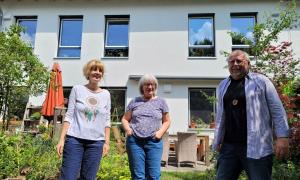 Zwei Frauen und ein Mann stehen vor einem Haus
