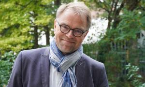 Ein Mann mit Brille und Schal, er lächelt