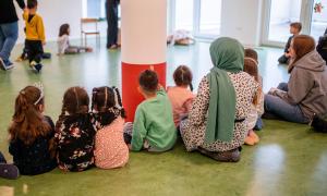 Kinder und Erzieherinnen sitzen auf dem Boden
