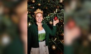 Eine Frau mit Krone auf dem Kopf steht neben einem Weihnachtsbaum