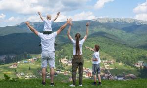 Eine vierköpfige Familie steht auf einem Berg und hebt die Arme in die Luft