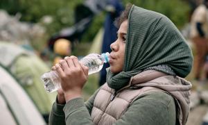 Ein Mädchen mit einem Kopftuch trinkt aus einer Wasserflasche