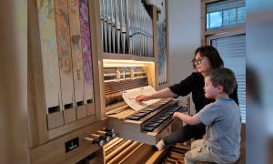 Ein Kind sitzt an einer Orgel, eine Frau steht neben ihm