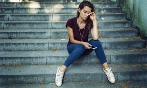 Eine Frau sitzt mit ihrem Handy auf einer Treppe, sie sieht müde und traurig aus