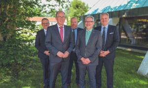 5 Männer in grauen Anzügen stehen auf einer grünen Wiese