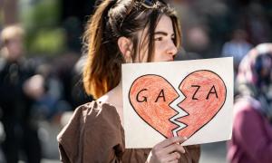 Eine junge Frau trägt ein kleines Plakat mit einem gebrochenen Herz und der Aufschrift “Gaza”