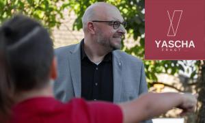 Ein Mann mit Brille und grauem Anzug lacht