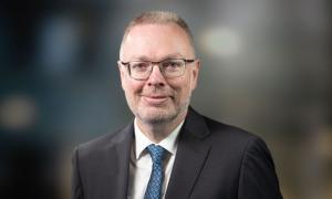 Ein Mann im Anzug mit Brille und kurzen Haaren lächelt