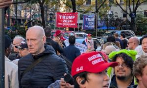 Mehrere Menschen besuchen eine Wahlkampfveranstaltung von Donald Trump und halten Schilder hoch