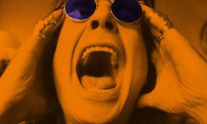Ein Mann mit Sonnenbrille reißt den Mund auf und hält sich die Finger an die Schläfen