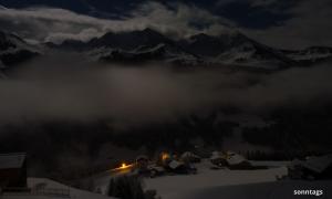 Ein Dorf in der Nacht vor wolkenumhangenen Bergen