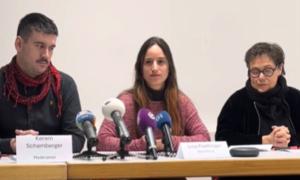 Eine junge Frau sitzt auf einem Podium mit Mikrofonen vor sich, links neben ihr ein Mann, rechts neben ihr eine Frau