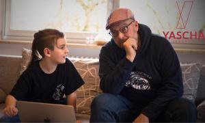 Ein Junge und ein Mann sitzen auf dem Sofa, vor sich ein Laptop