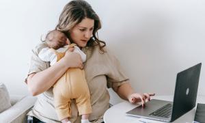 Eine Frau mit einem kleinen Kind auf dem Arm sitzt am Laptop