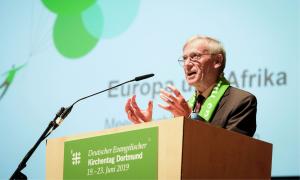 Ein Mann steht an einem Rednerpult, er hat einen grünen Schal um die Schultern