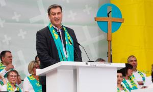 Ein Mann mit umgehängtem Schal spricht vor einem Kreuz