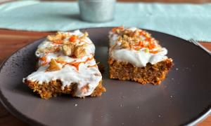 Ein Teller mit zwei kleinen Stücken Karottenkuchen. Auf dem Kuchen ist weißes Frosting, Karottelrapseln und kleine Wallnüssstücke.