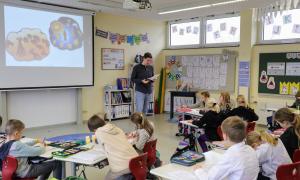 Ein Klassenzimmer, in dem sehr junge Schülerinnen und Schüler sitzen, vorne steht ein Lehrer