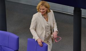 Eine Frau in einem beigen Anzug steht hinter einem Stuhl