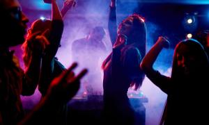 Menschen tanzen im Discolicht, im Hintergrund ein DJ