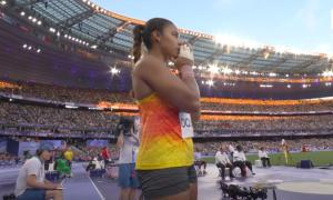 Eine Frau in Sportbekleidung im Stadion, sie faltet die Hände vor dem Mund