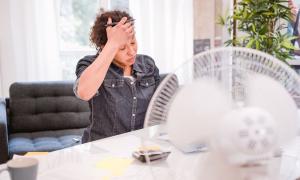 Eine Frau sitzt am Schreibtisch, vor ihr ein Ventilator