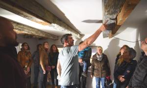 Menschen stehen in einem Raum und schauen auf einen alten Balken an der Decke